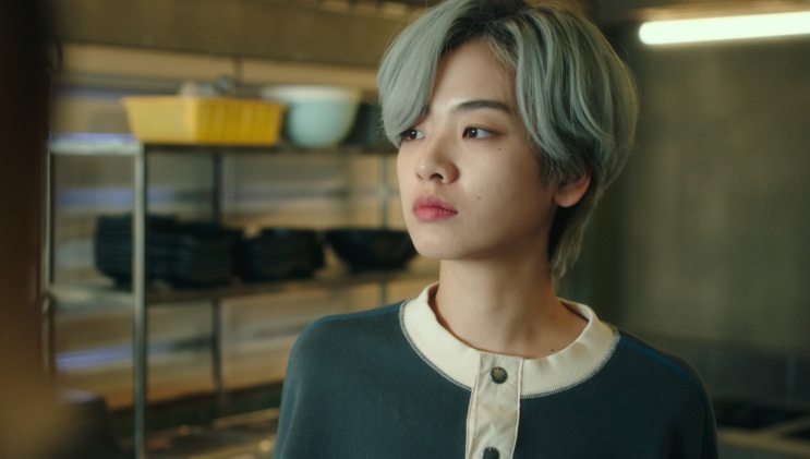 Ma Hyun-yi de blusa escura, olhando para o lado na cozinha do Danbam