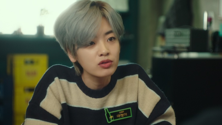 Ma Hyun-yi de blusa listrada, falando em um ambiente interno