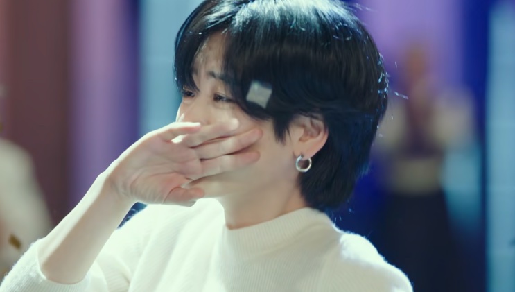 Ma Hyun-yi de blusa branca, enxugando o rosto com a mão