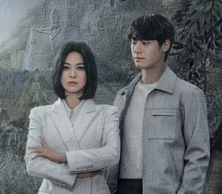Song Hye-kyo de terno claro e Lee Do-hyun de jaqueta cinza, lado a lado, em A Lição