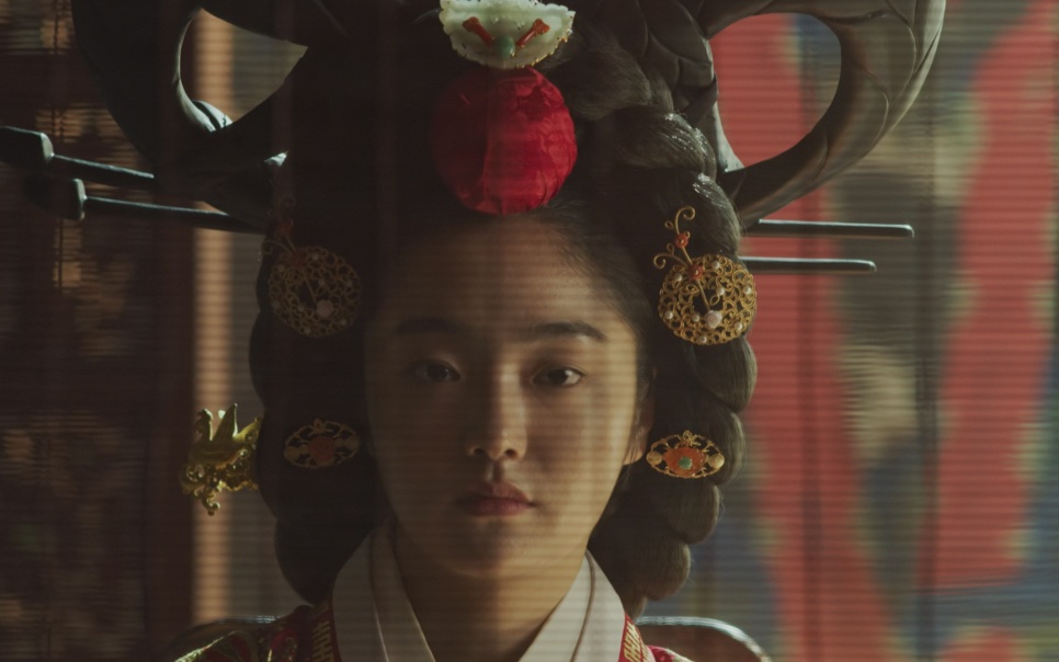A rainha de Kingdom com o penteado cerimonial alto e um enfeite vermelho no alto da cabeça