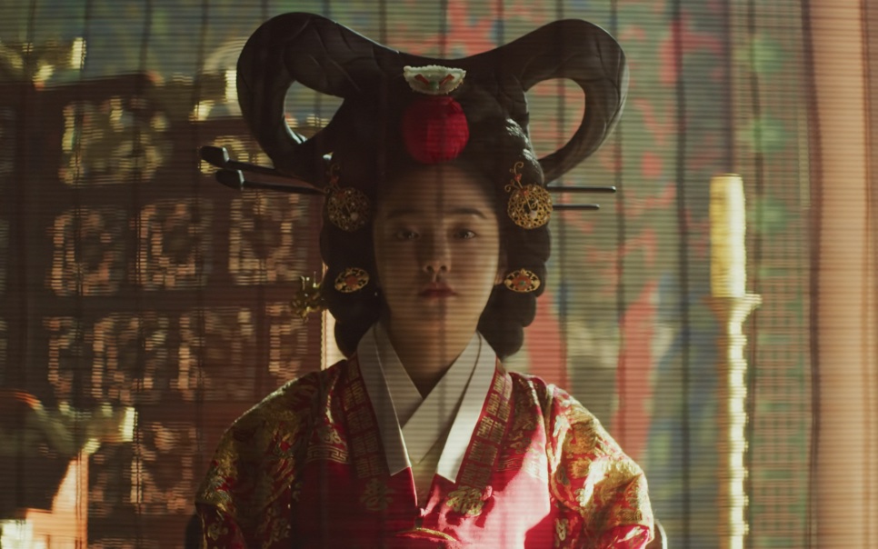 A rainha de Kingdom sentada no salão do palácio, de roupa vermelha e penteado cerimonial