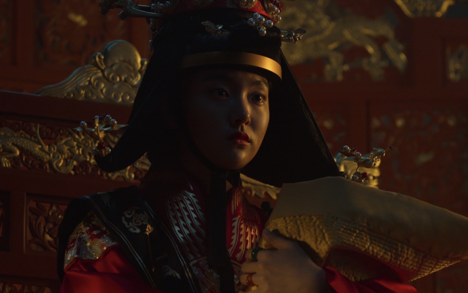 A rainha de Kingdom sentada no trono com um chapéu preto e dourado e roupa vermelha