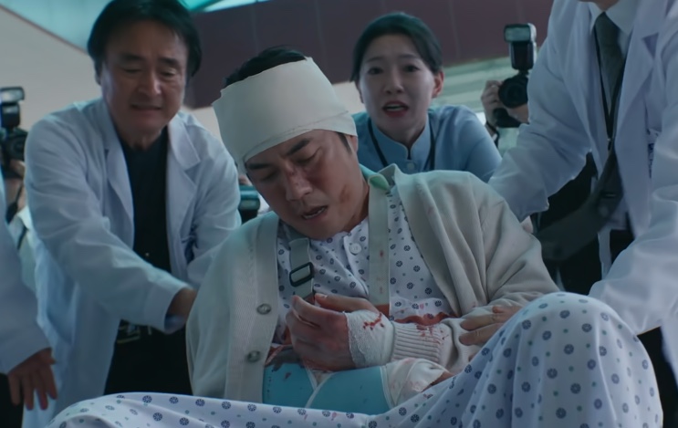 Ju Gang-chan ferido e sangrando, amparado por médicos