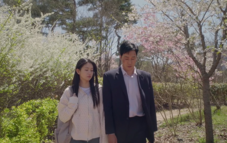 Kim e a filha Minji caminhando juntos entre cerejeiras floridas