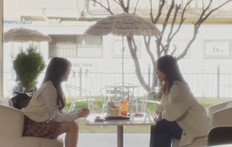 Jung Sang-a e Minji conversando numa mesa de café ao ar livre