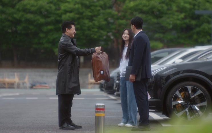Im Ho-won entregando uma pasta de couro a Kim e Minji num estacionamento