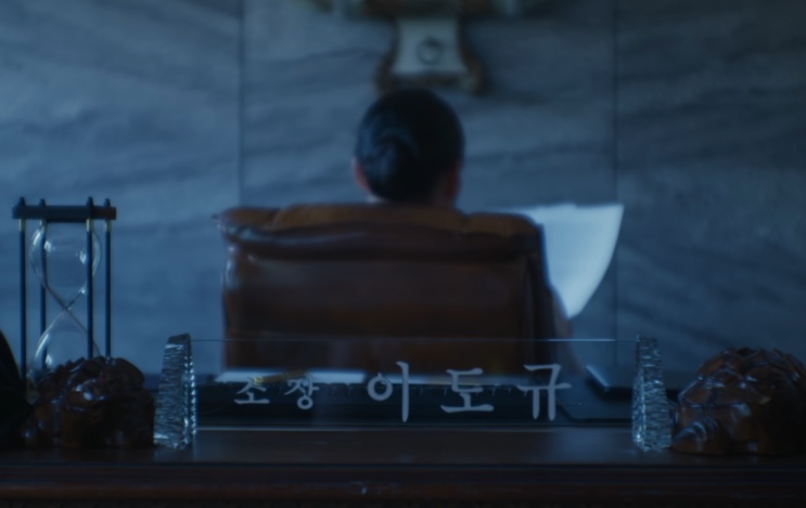 Uma cadeira de escritório de costas e uma placa de mesa com o nome do diretor Lee Do-gyu