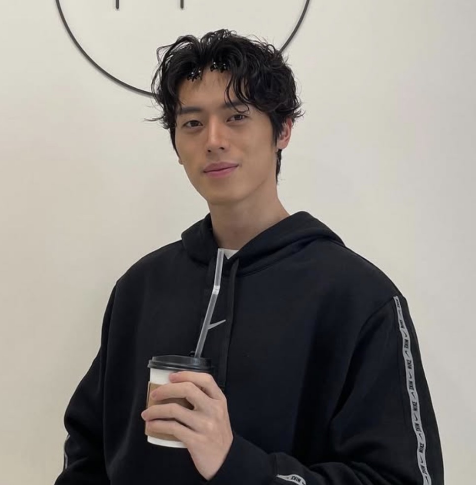 Lee Joo-ahn de moletom preto, sorrindo com um copo de café na mão