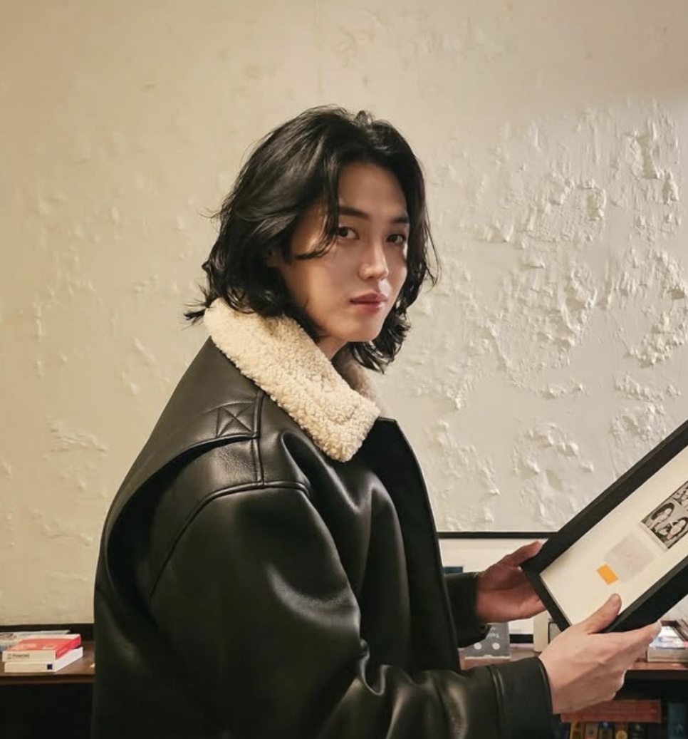 Lee Joo-ahn de cabelo comprido e jaqueta de couro preta com gola de pelúcia, segurando um quadro