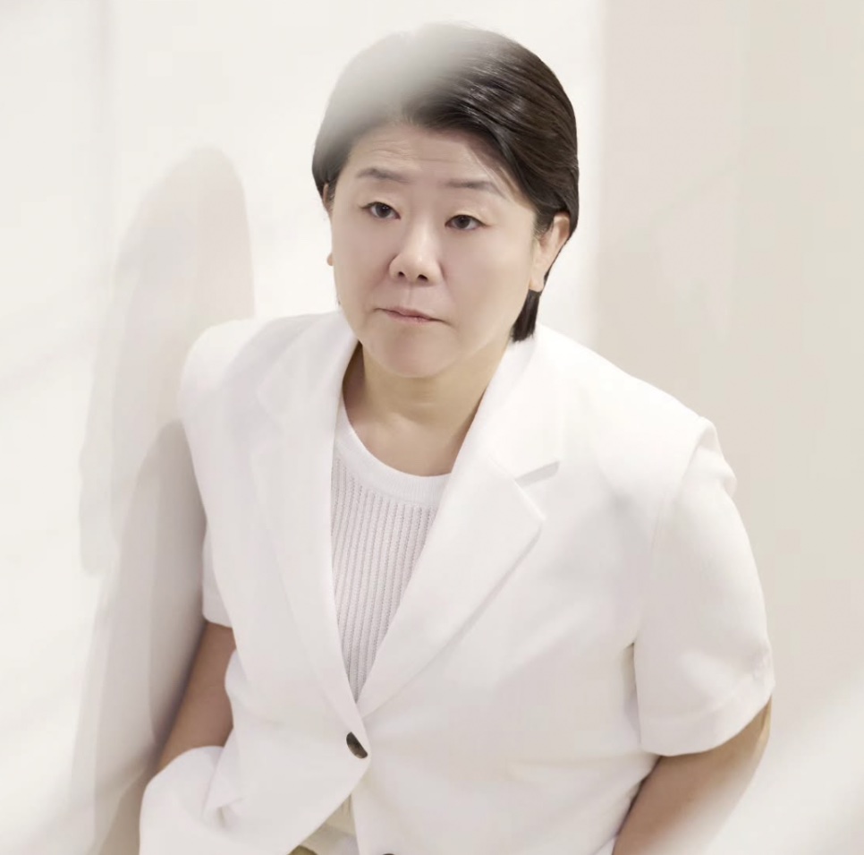 Lee Jung-eun de blazer branco, encostada numa parede clara