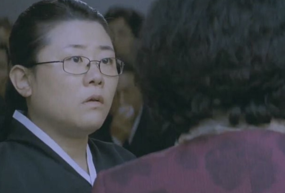 Lee Jung-eun jovem, de óculos e roupa preta, em uma cena do filme Mother: A Busca pela Verdade