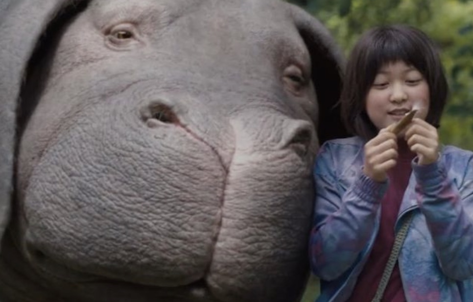 A superporca Okja, de perto, ao lado da menina que cuida dela, no filme Okja