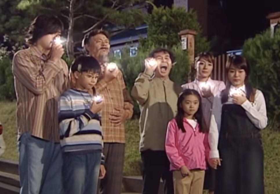 A família de bruxos de Magic Kid Masuri reunida à noite em frente a uma casa, cada um com uma luz na mão
