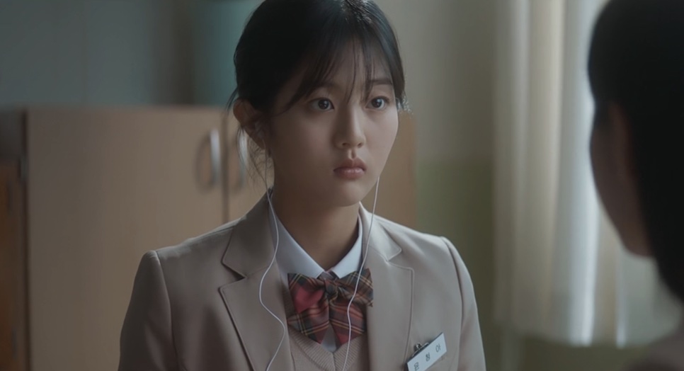 Yoon Cheong-a de uniforme escolar, com fones de ouvido, olhando para alguém à frente