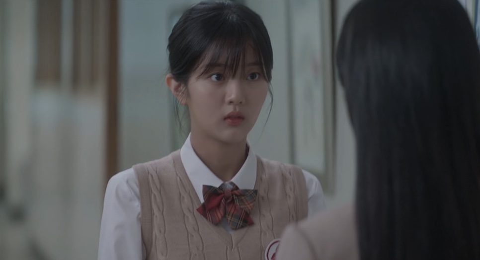 Yoon Cheong-a de colete bege e laço no uniforme, de frente para uma garota de cabelo comprido