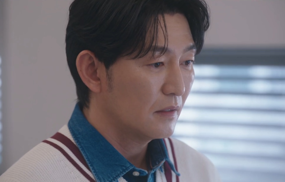 Close do Choi Seong-uk de colete branco com listras vinho, olhando para baixo com expressão tensa