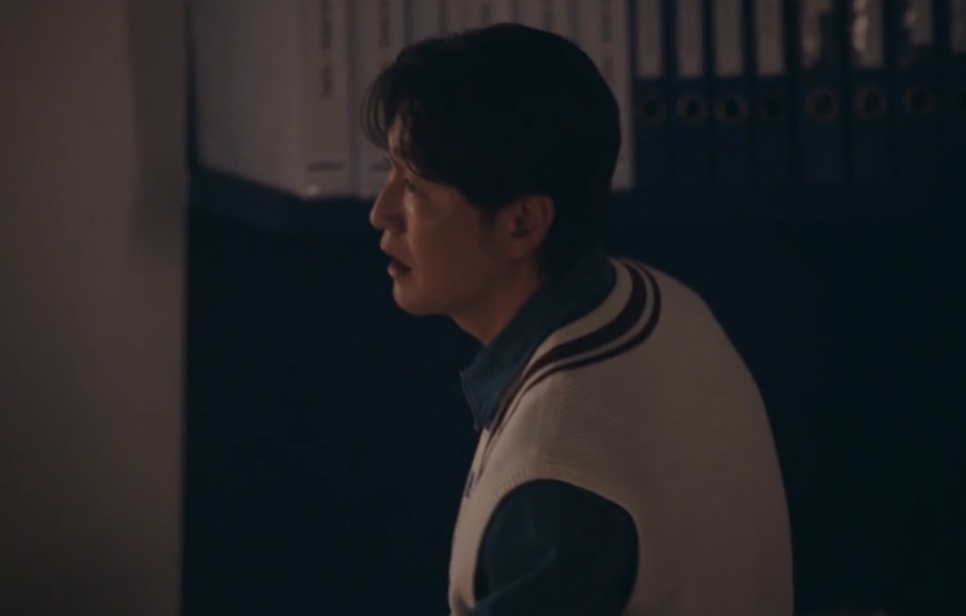 Choi Seong-uk de colete, olhando para o lado num corredor escuro