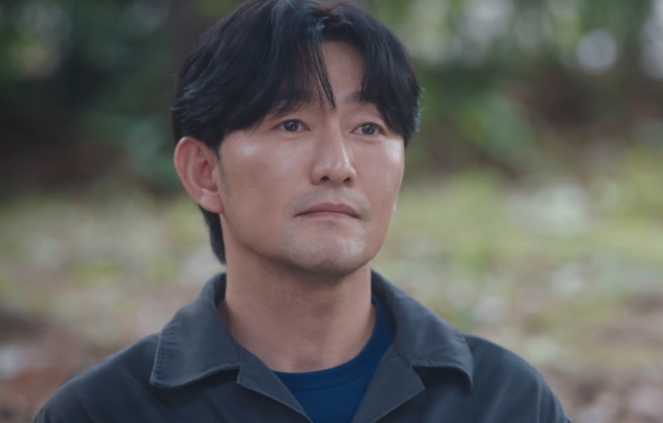 Choi Seong-uk de jaqueta de trabalho escura, ao ar livre, com os olhos marejados