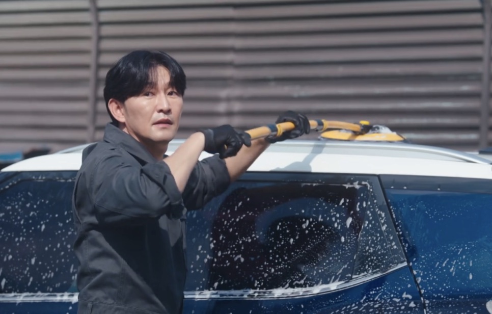 Choi Seong-uk de luvas, lavando um carro azul coberto de espuma num lava-jato