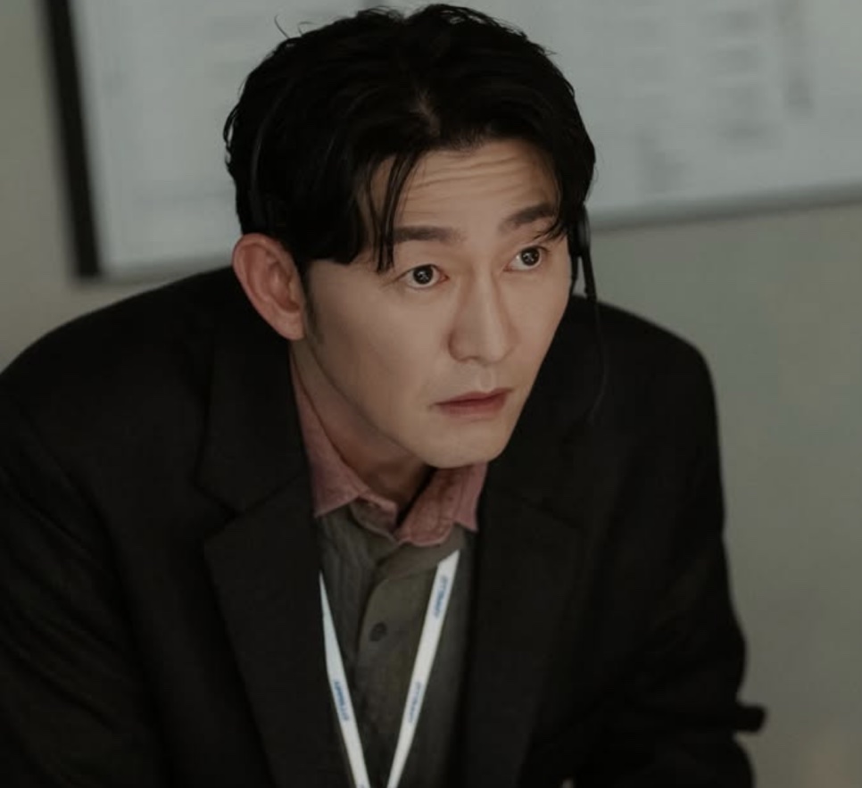 Heo Joon-seok de blazer preto e crachá no pescoço, no papel do Choi Seong-uk