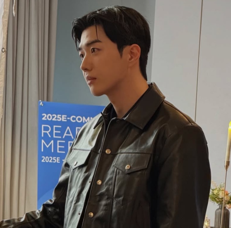 Kang Ha-gi de jaqueta de couro preta, de perfil, num salão de evento