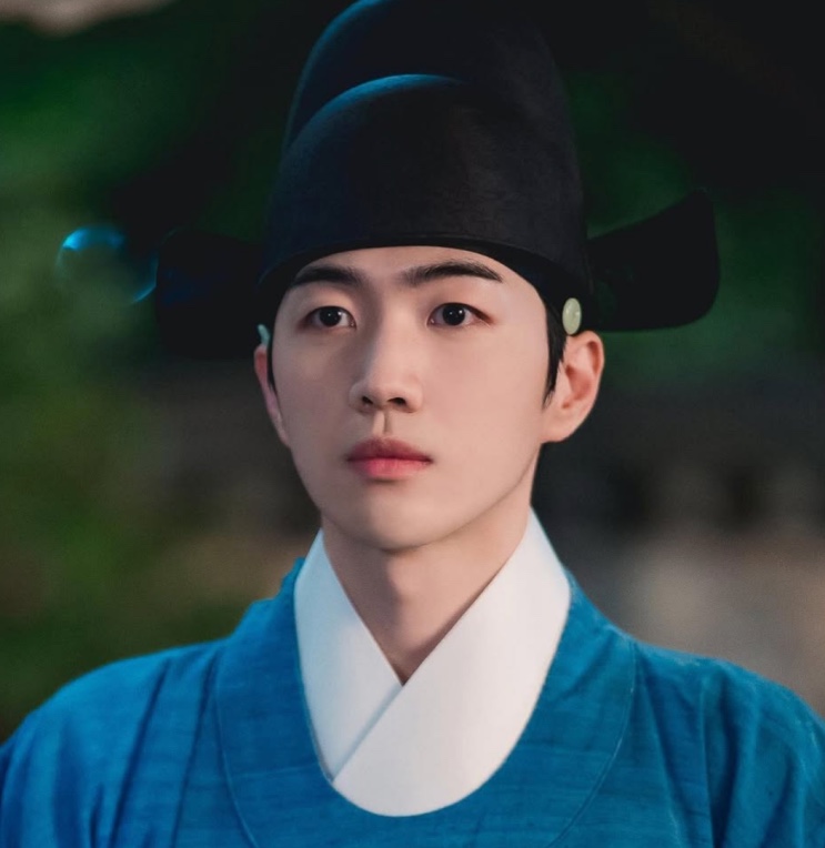 Kang Hoon de traje azul da corte, à noite, olhando para a câmera