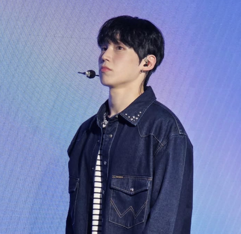 Chun Woo-jin, o ator que faz o Roy, de jaqueta jeans escura no palco, com luz roxa atrás