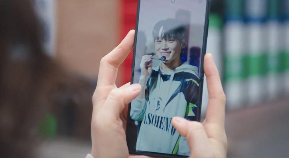 Duas mãos segurando um celular com a foto de um idol sorrindo no palco