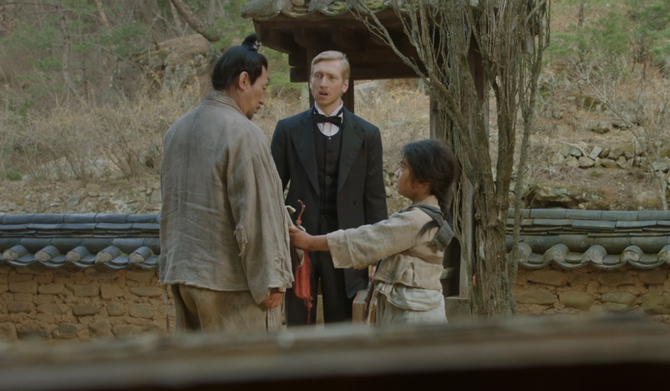 Joseph Stenson em um vilarejo coreano, entre um homem e um menino