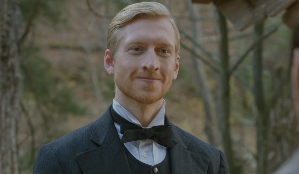 Joseph Stenson sorrindo ao ar livre, com árvores ao fundo