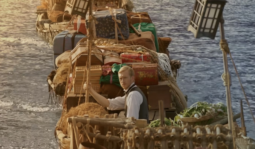 Joseph Stenson em um barco carregado de malas e caixas, atravessando um rio