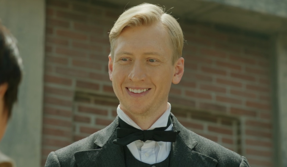 Joseph Stenson sorrindo em frente a uma parede de tijolos