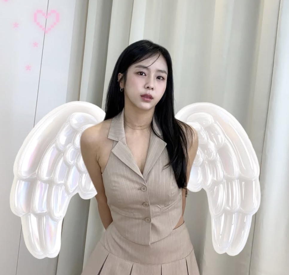 Yewon de colete e saia bege, posando com asas de anjo brancas presas nas costas
