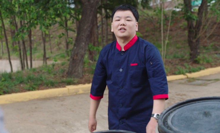 Kwaktube de pé, de jaleco de cozinha, em uma via do quartel
