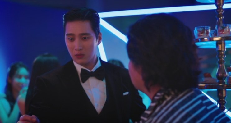 Homem de smoking conversando em um evento de lançamento, com convidados ao redor