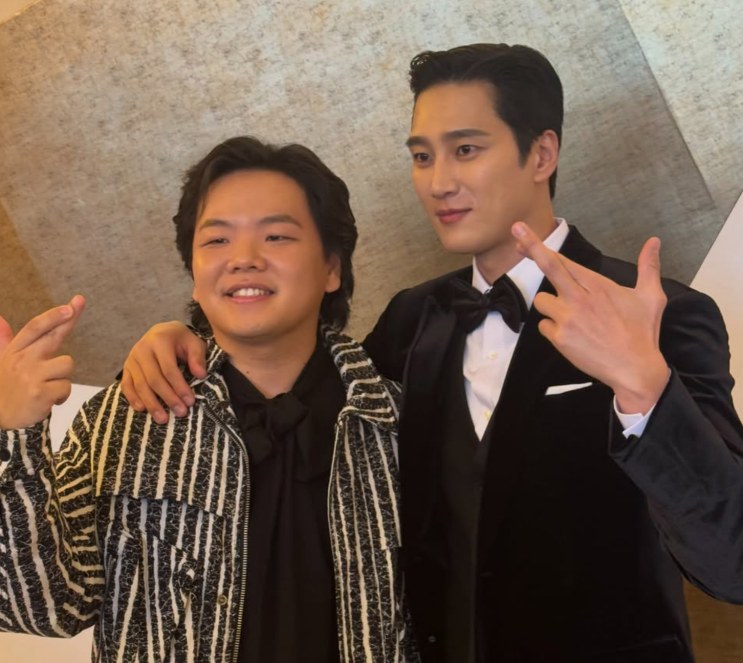Kwaktube e Ahn Bo-hyun posando juntos nos bastidores, um de paletó listrado e o outro de smoking