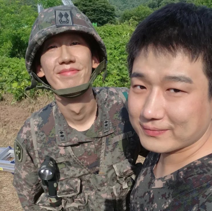 Nam Tae-woo e um colega de uniforme e capacete, lado a lado em uma selfie no campo