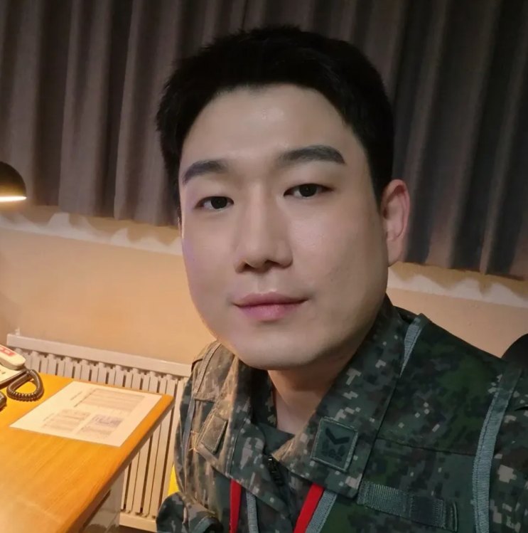 Nam Tae-woo de uniforme camuflado em uma selfie dentro de uma sala