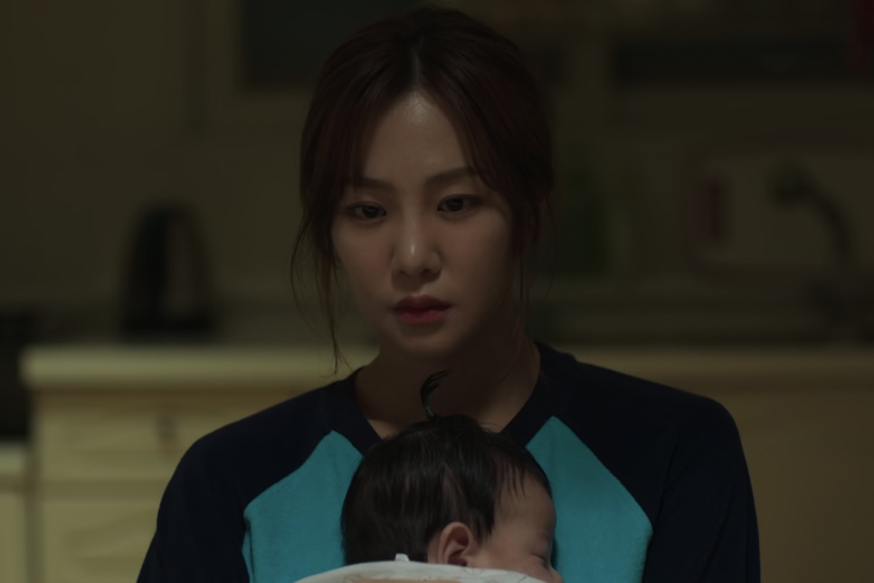 A Han-ju com um bebê no colo, numa cozinha à noite