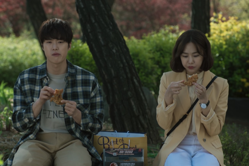 A Han-ju e o Jae-hun sentados num banco ao ar livre, comendo frango frito