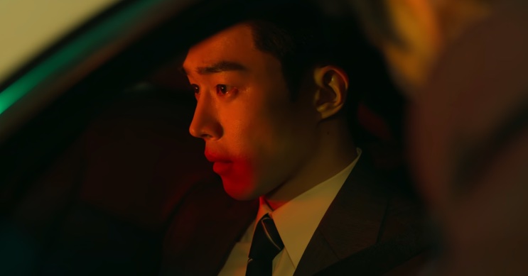 Son Soo-hyun de perfil dentro de um carro, sob luz avermelhada