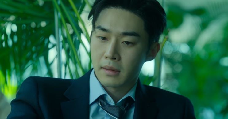 Son Soo-hyun sentado de terno, olhando para baixo