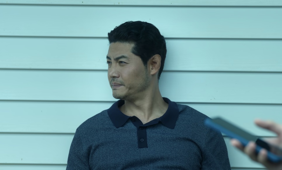 O detetive Dong-cheol encostado em uma parede azul-clara, olhando para o lado