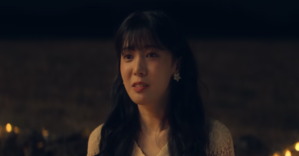 So Min-yeong falando à noite, de brinco grande e blusa clara