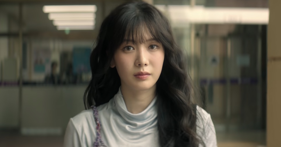 Close da So Min-yeong de blusa clara de gola alta, em um corredor iluminado