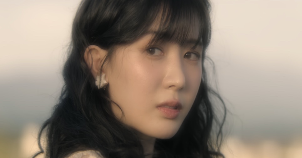 So Min-yeong olhando para trás por cima do ombro, com o céu claro ao fundo
