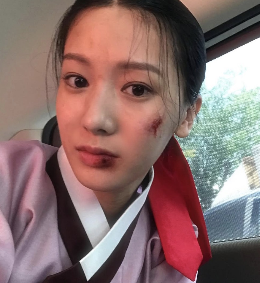 Song Su-yi de hanbok rosa, com maquiagem de ferimento no rosto, em selfie de bastidores de The Haunted Palace
