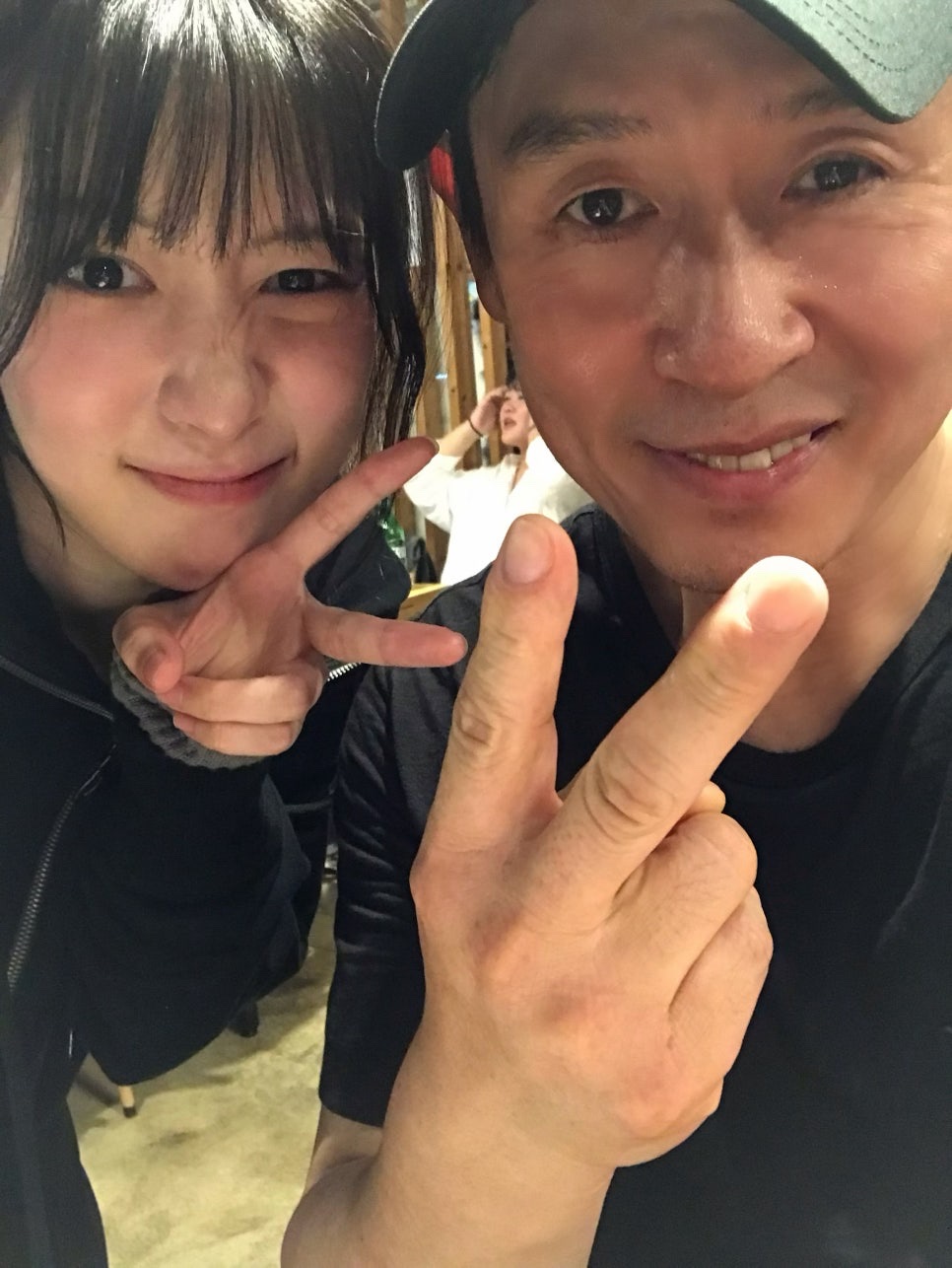 Song Su-yi fazendo sinal de paz em selfie com um ator de boné, nos bastidores