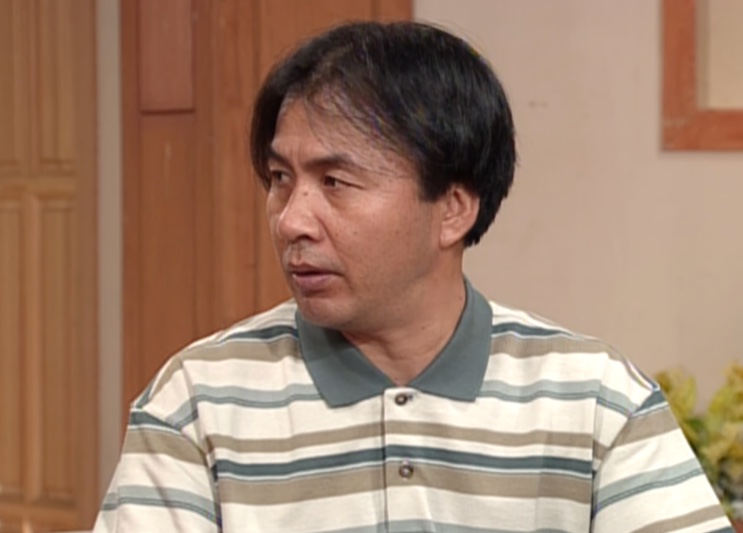 Oh Ji-myung de camisa polo listrada, com expressão de quem está discutindo